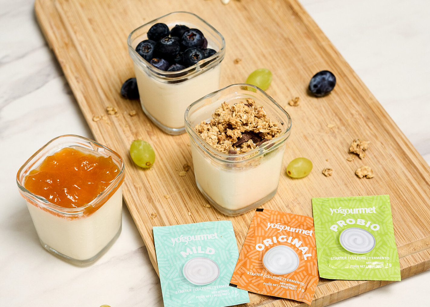 Yogourmet products arranged with yoghurt cups on a wooden board